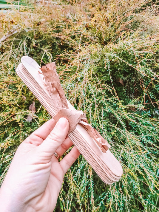 Hand holding a wooden comb against a natural background of green and brown foliage.