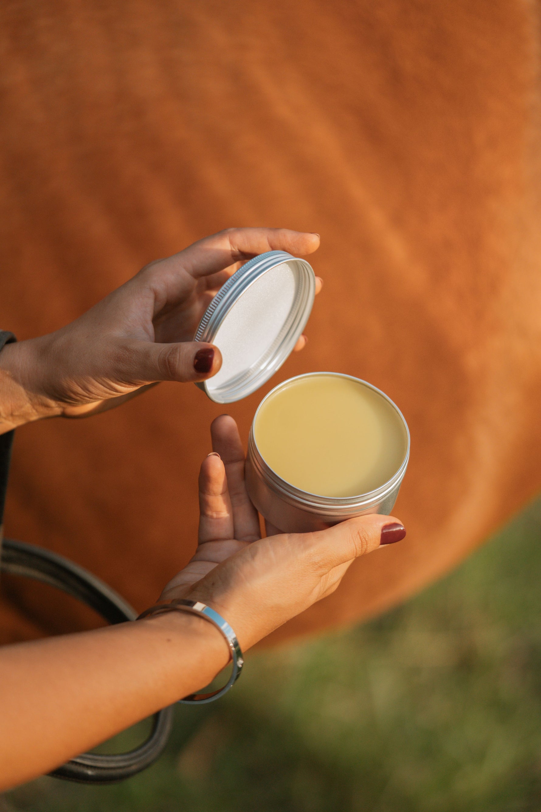 Person holding Bees Knee's Leather Balm open with horse in background