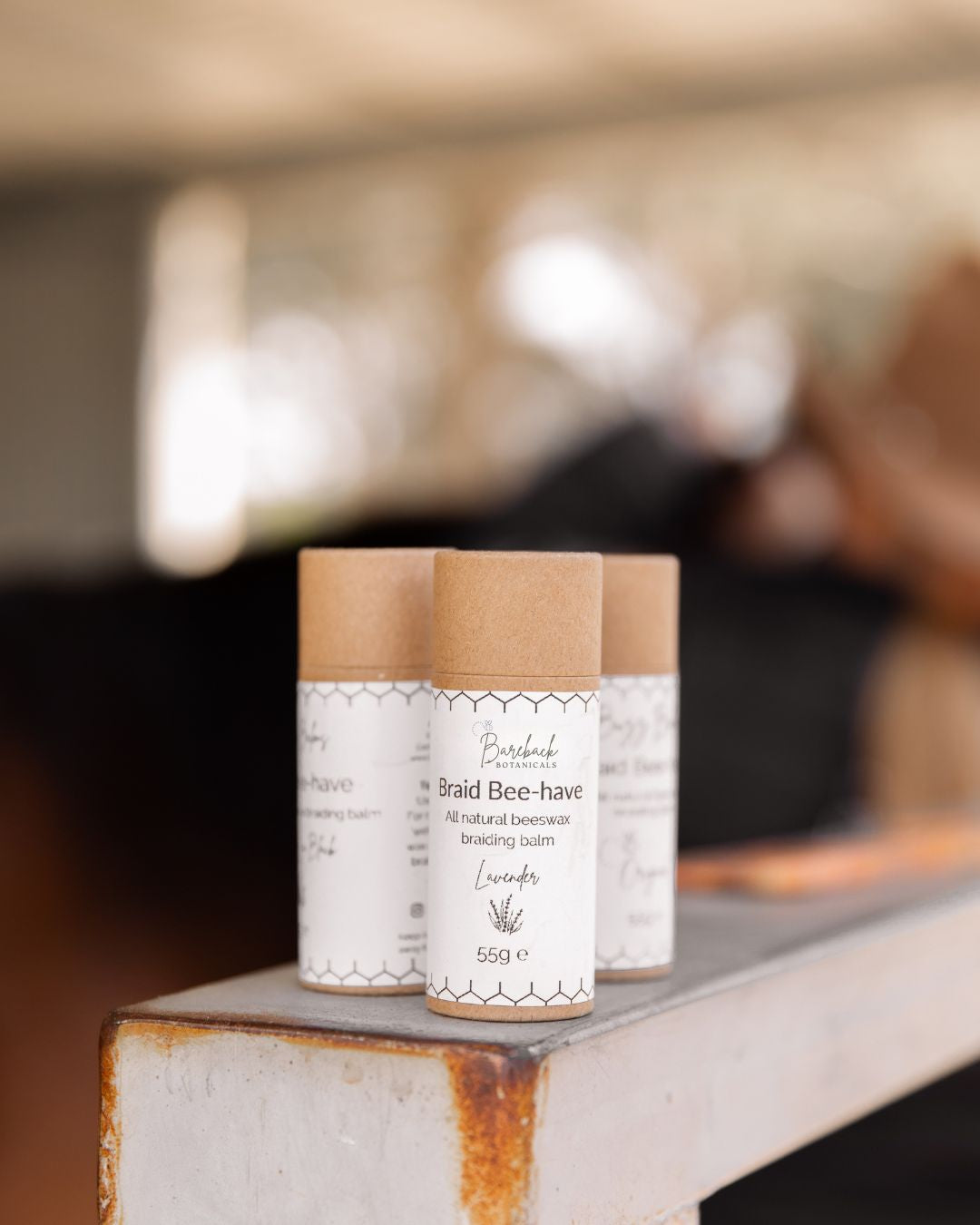 Three tubes of Bareback Botanical's 'Braid Beehave' on a metal surface with a blurred background.