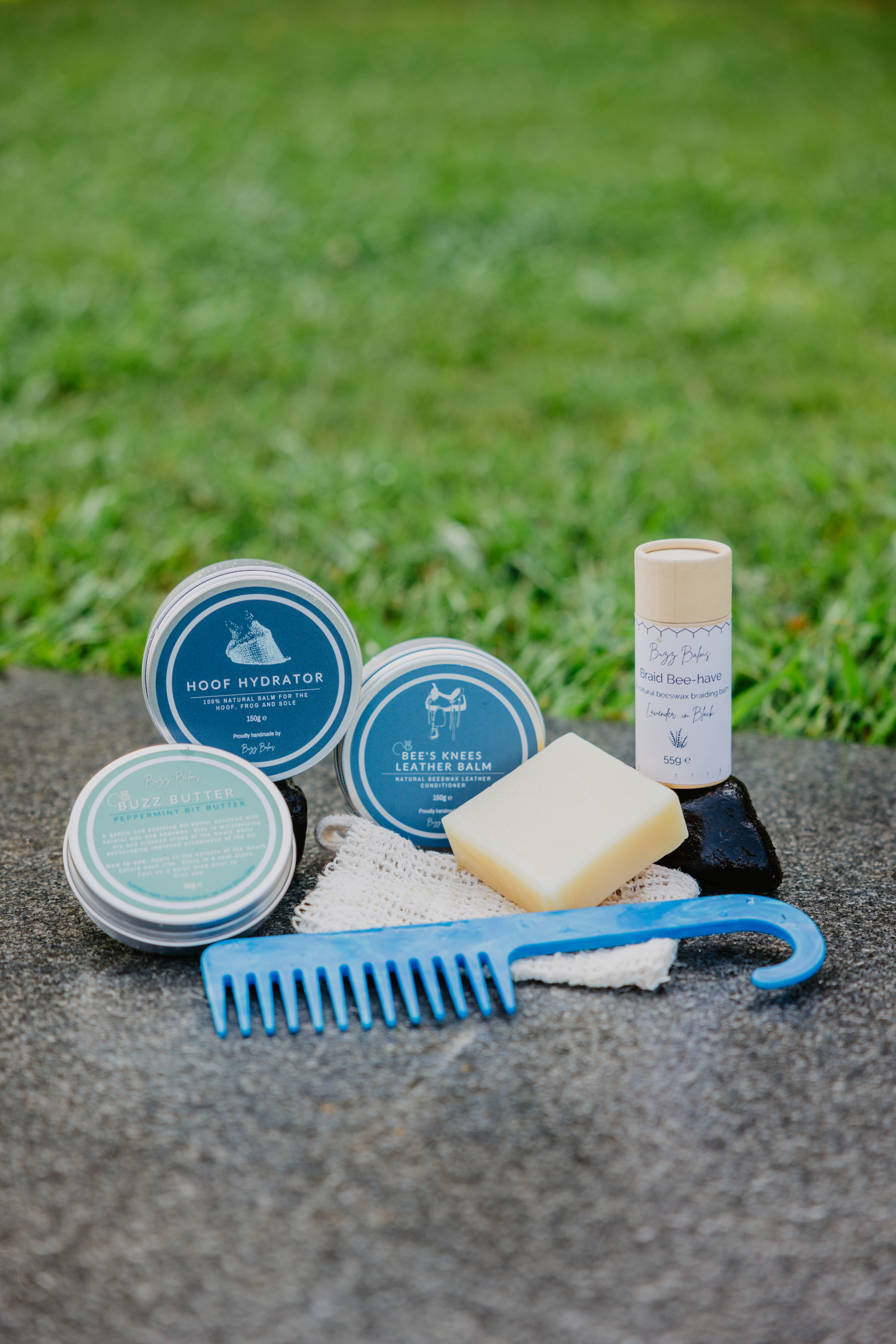 Grooming products including a comb, soap, and other items on a stone surface with grass in the background.